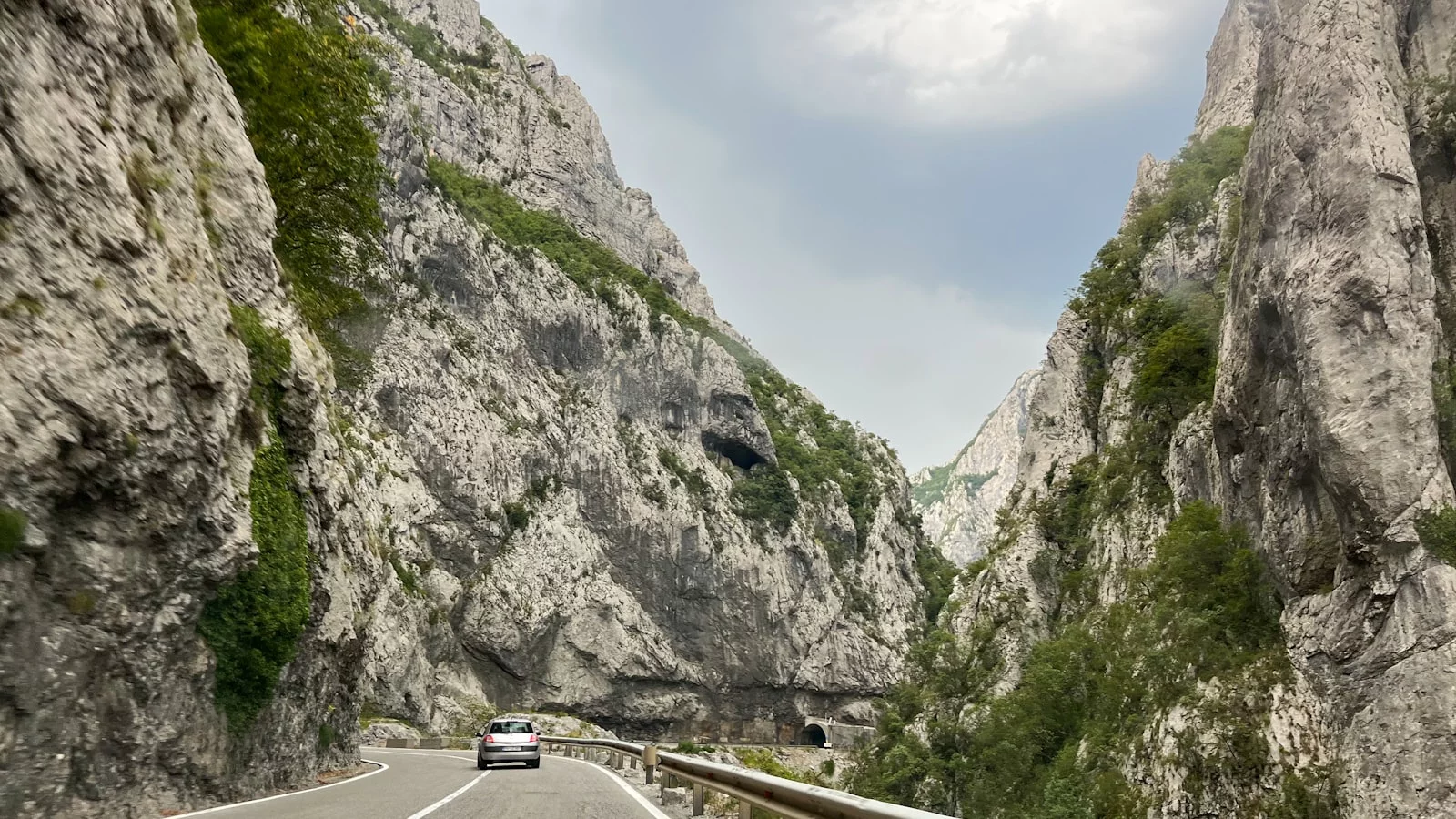 Voiture sur une route monténégrine encaissée entre de hautes falaises rocheuses.