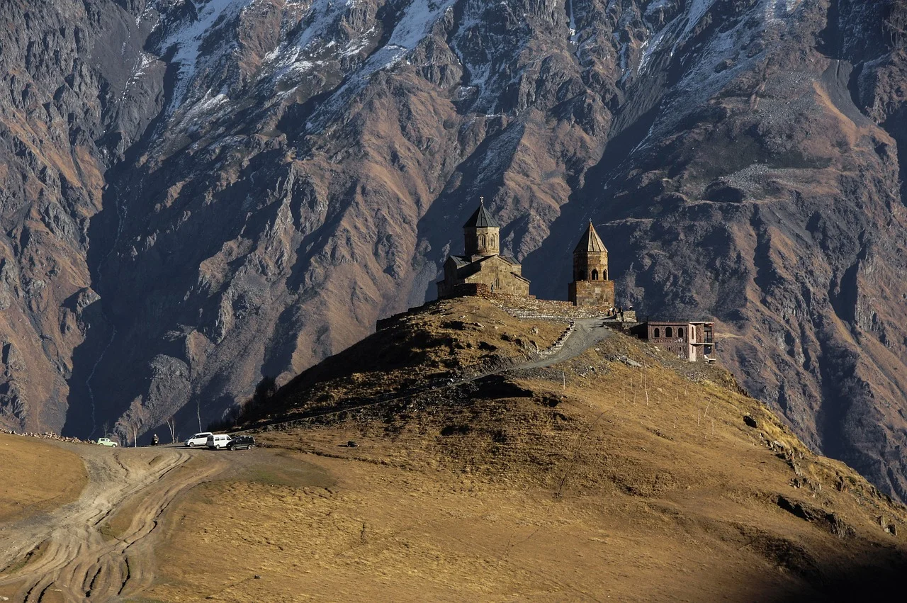L'église de la Trinité de Gergeti sur son promontoire herbeux, devant les immenses parois du Grand Caucase géorgien