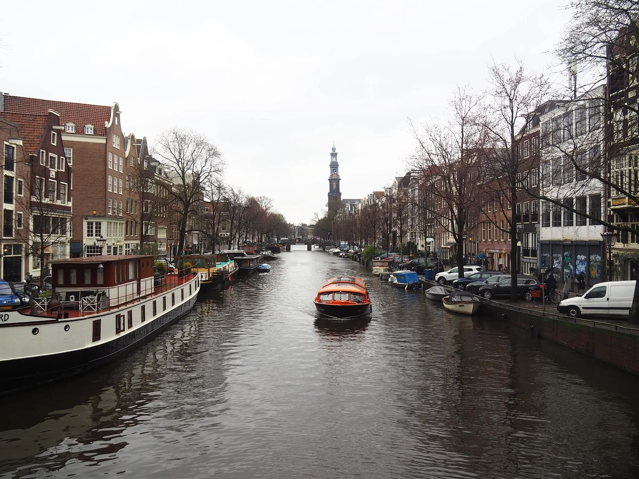 Canal d'Amsterdam bordé de maisons à pignons, avec un bateau de tourisme orange et la tour de la Westerkerk au fond
