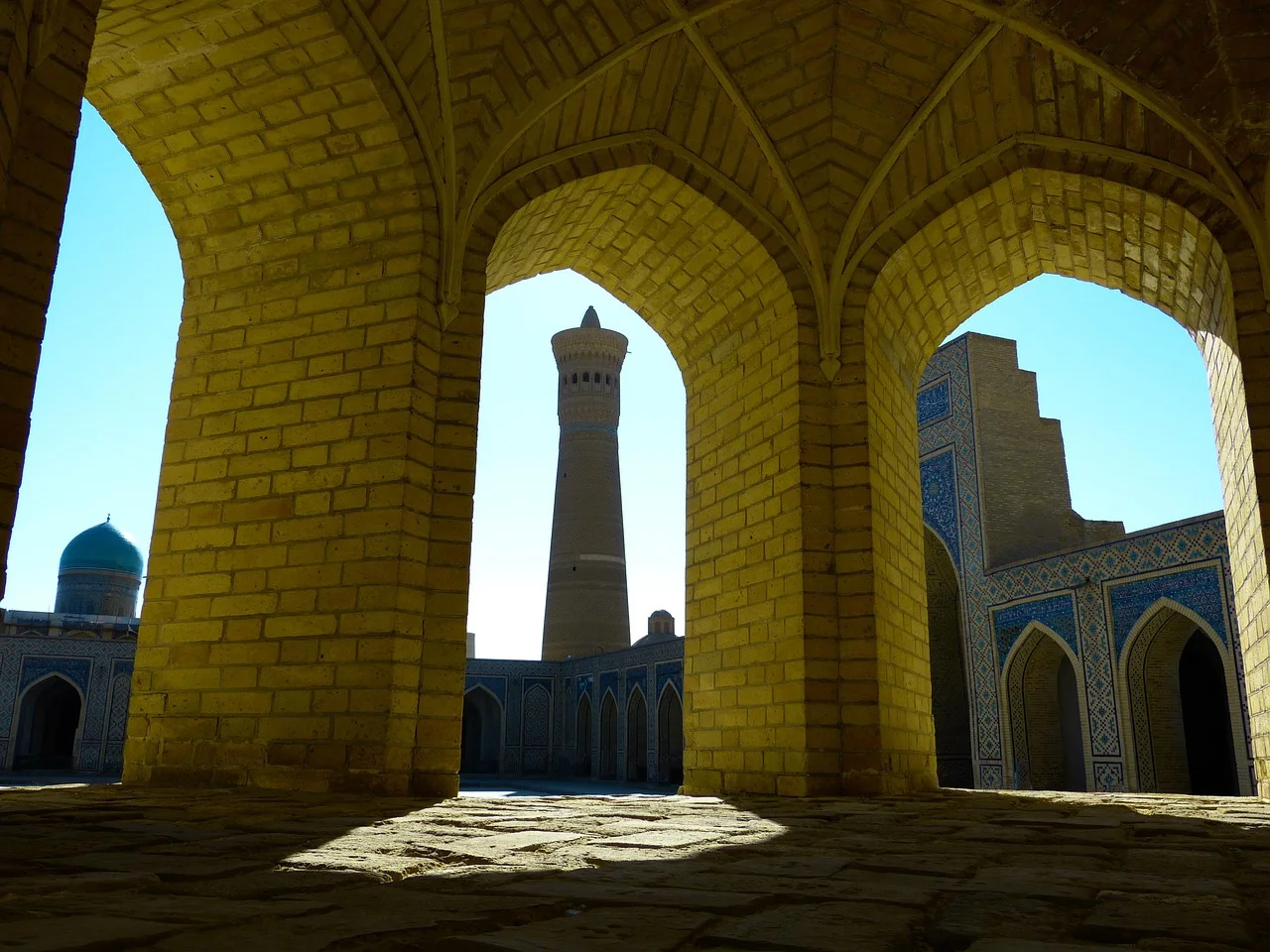 Le minaret Kalon de Boukhara en Ouzbékistan encadré par les arches de brique de la mosquée Kalon, avec une façade de mosaïque bleue sur la droite