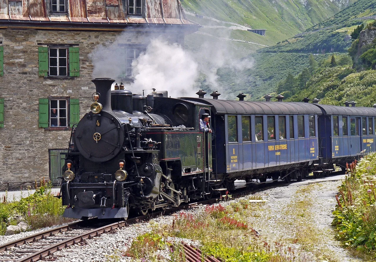 Locomotive à vapeur noire tractant des wagons bleus sur la ligne de la Furka, dans les Alpes suisses.