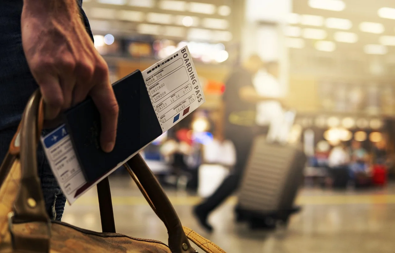 Passport and boarding pass held in one hand in front of an airport concourse