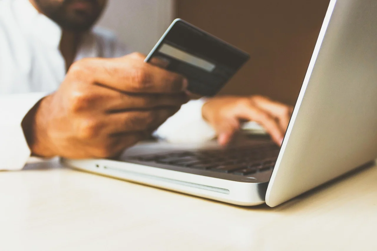 Person holding a bank card in front of a laptop to make an online payment