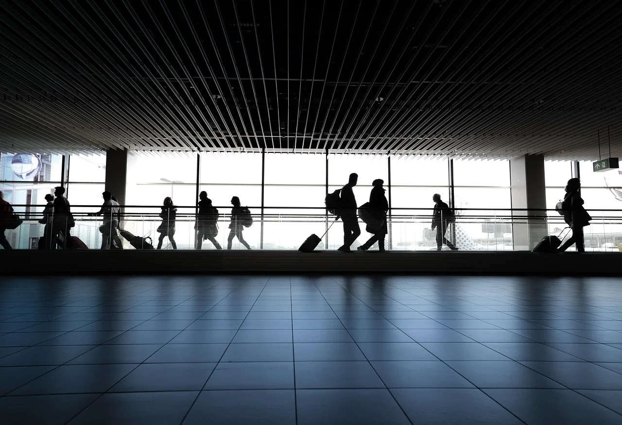 Silhouettes of travellers with suitcases crossing a glass airport walkway