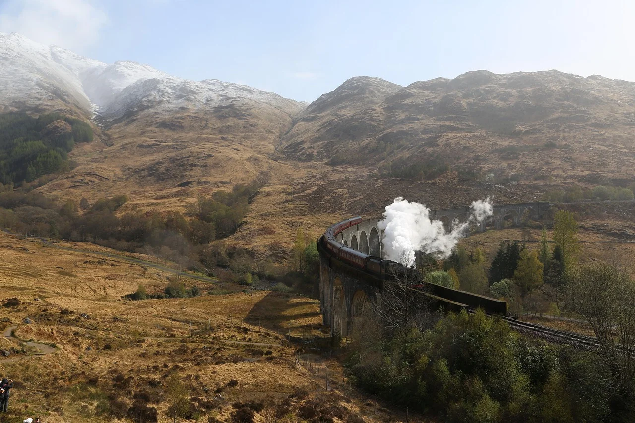 Train à vapeur franchissant un viaduc de pierre en courbe au cœur d'une lande de montagne.