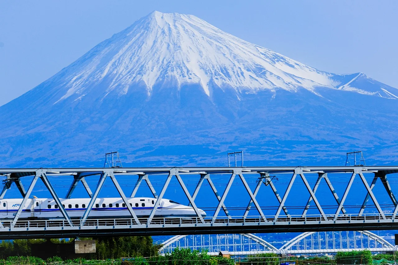 Un Shinkansen blanc franchit un pont métallique avec le mont Fuji enneigé en arrière-plan.