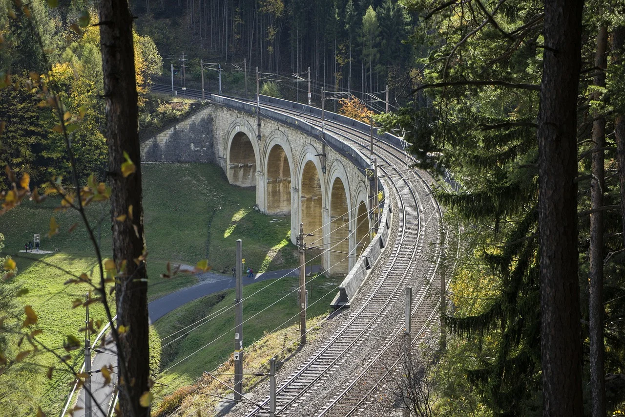 Viaduc ferroviaire en pierre du Semmering dessinant une courbe au milieu de la forêt autrichienne.