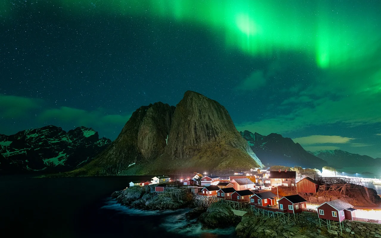 Aurore boréale verte au-dessus des cabanes rouges de pêcheurs de Hamnøy, dans les îles Lofoten en Norvège, sous un ciel étoilé.