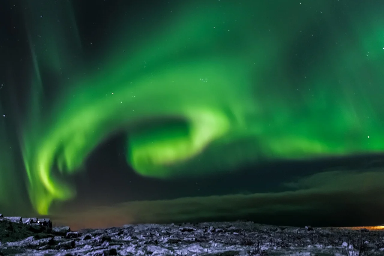 Aurore boréale verte en forme de spirale au-dessus d'un champ de lave enneigé en Islande, sous un ciel étoilé.