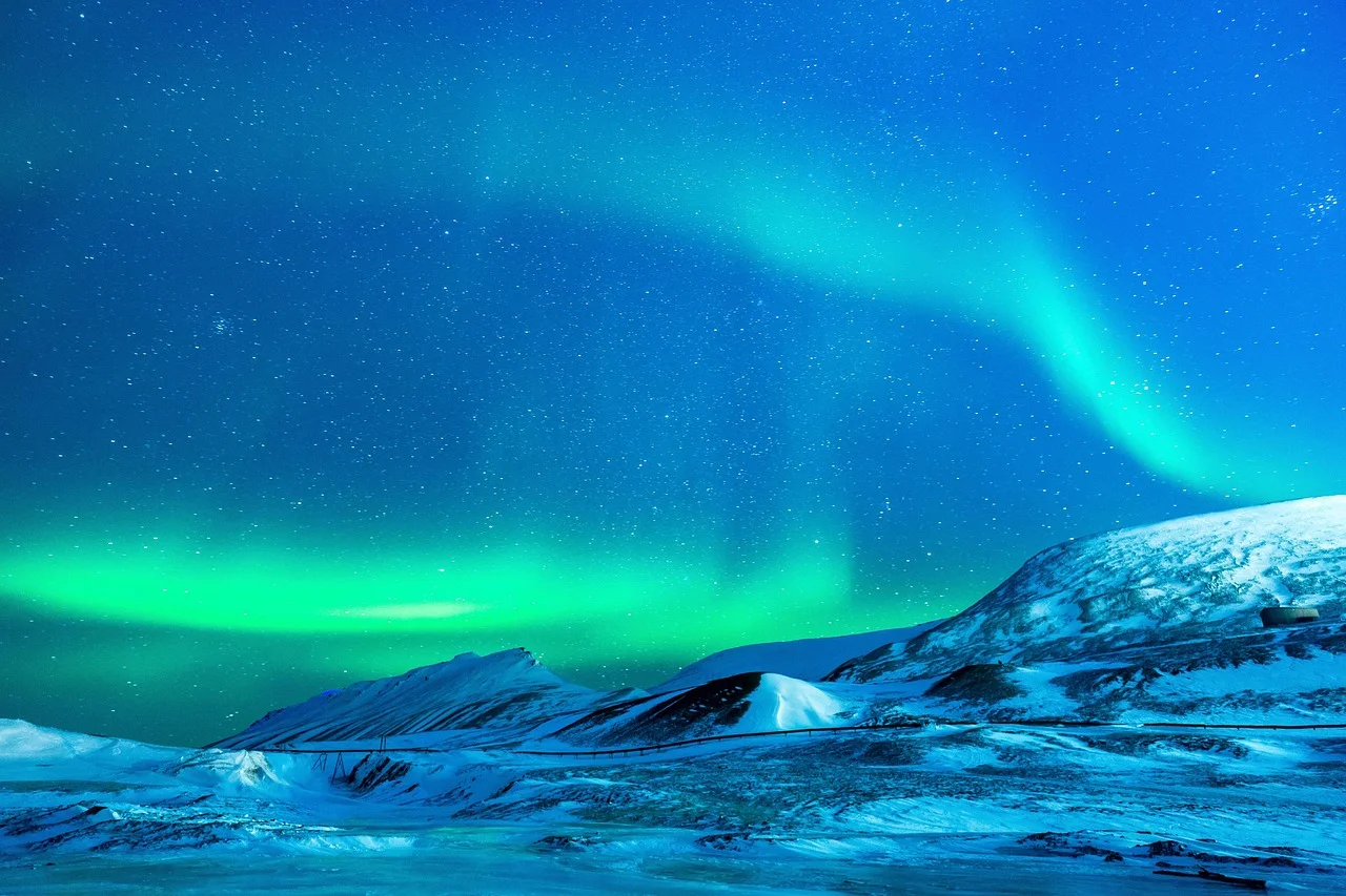 Aurore boréale verte et bleue au-dessus de collines enneigées sous un ciel constellé d'étoiles, par temps parfaitement dégagé.