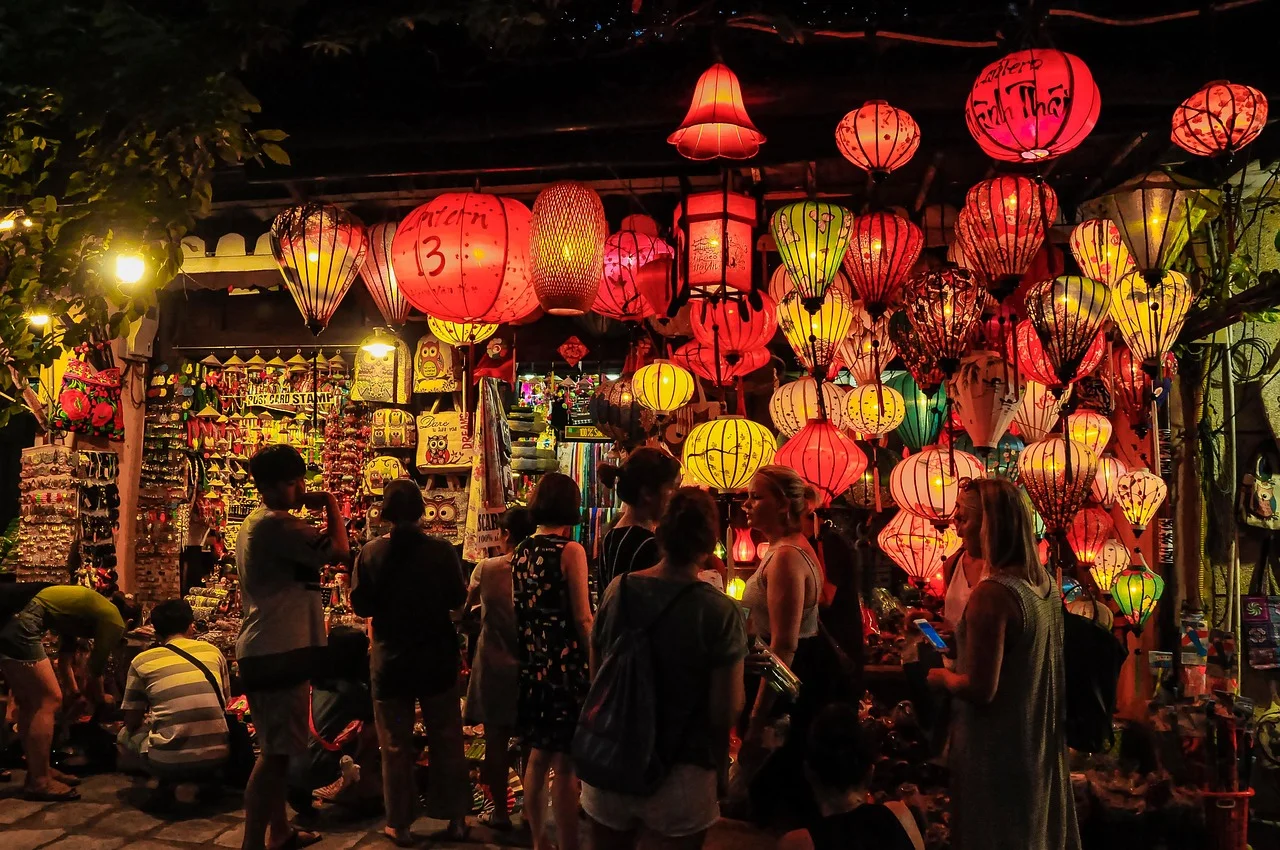 Boutique de lanternes en soie multicolores illuminées la nuit dans la vieille ville de Hoi An, avec des passants devant l'étal.