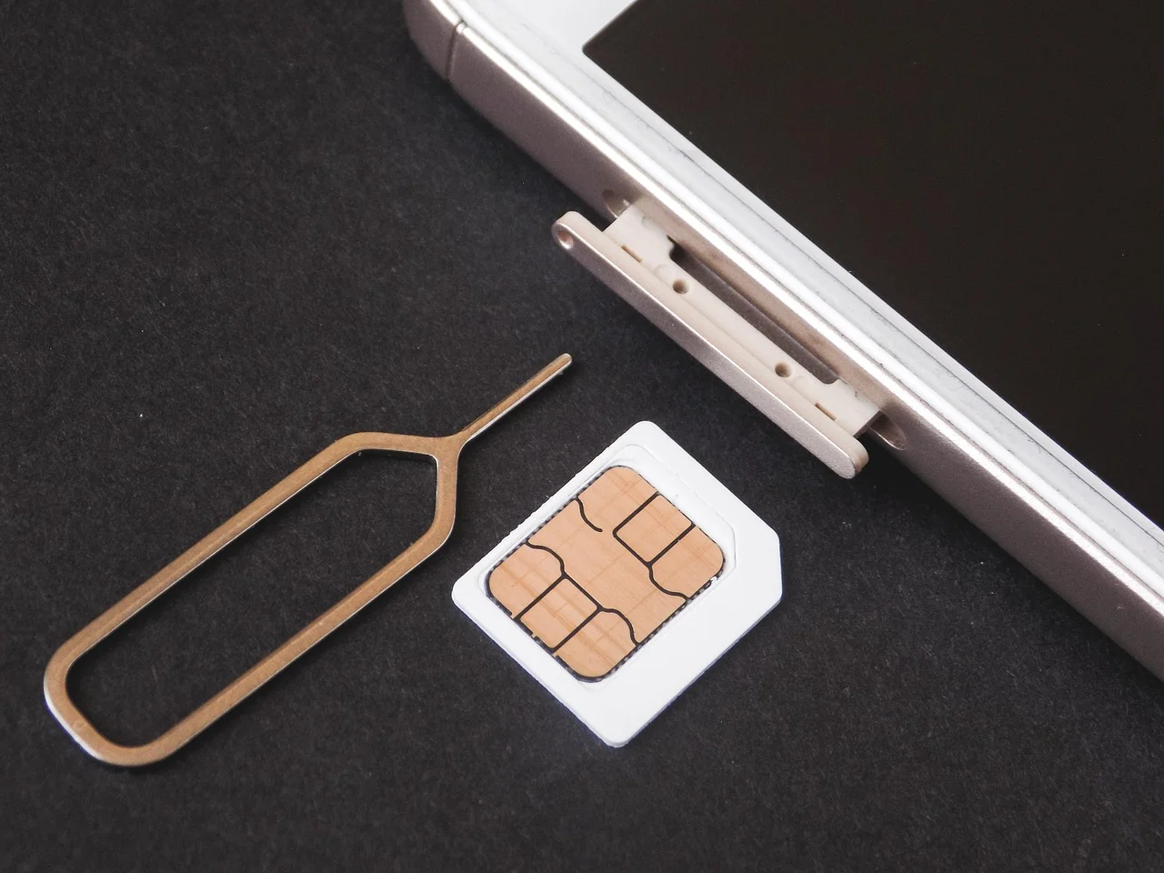 Carte nano-SIM, outil d'éjection et tiroir SIM sorti d'un smartphone blanc, posés sur un fond sombre