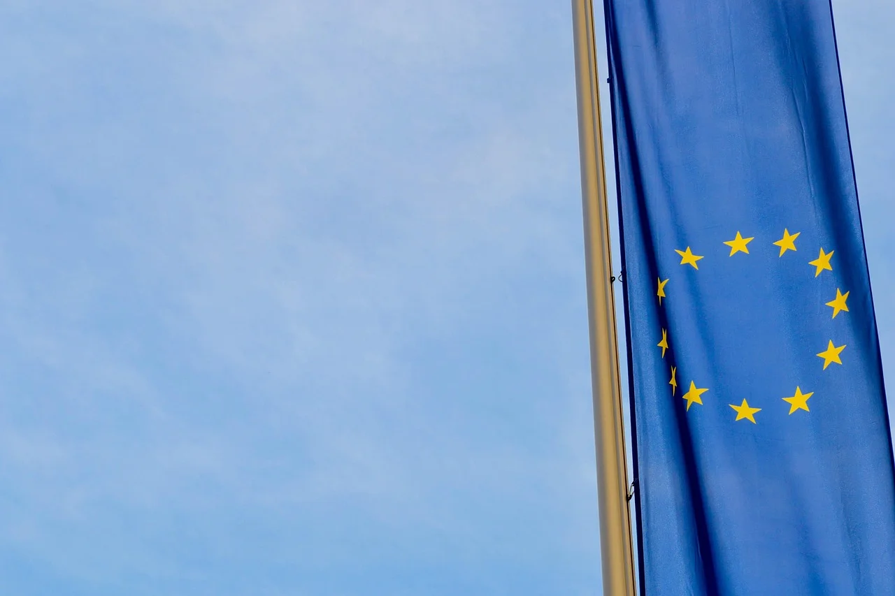 Drapeau de l'Union européenne bleu aux douze étoiles jaunes flottant sur un mât devant un ciel clair