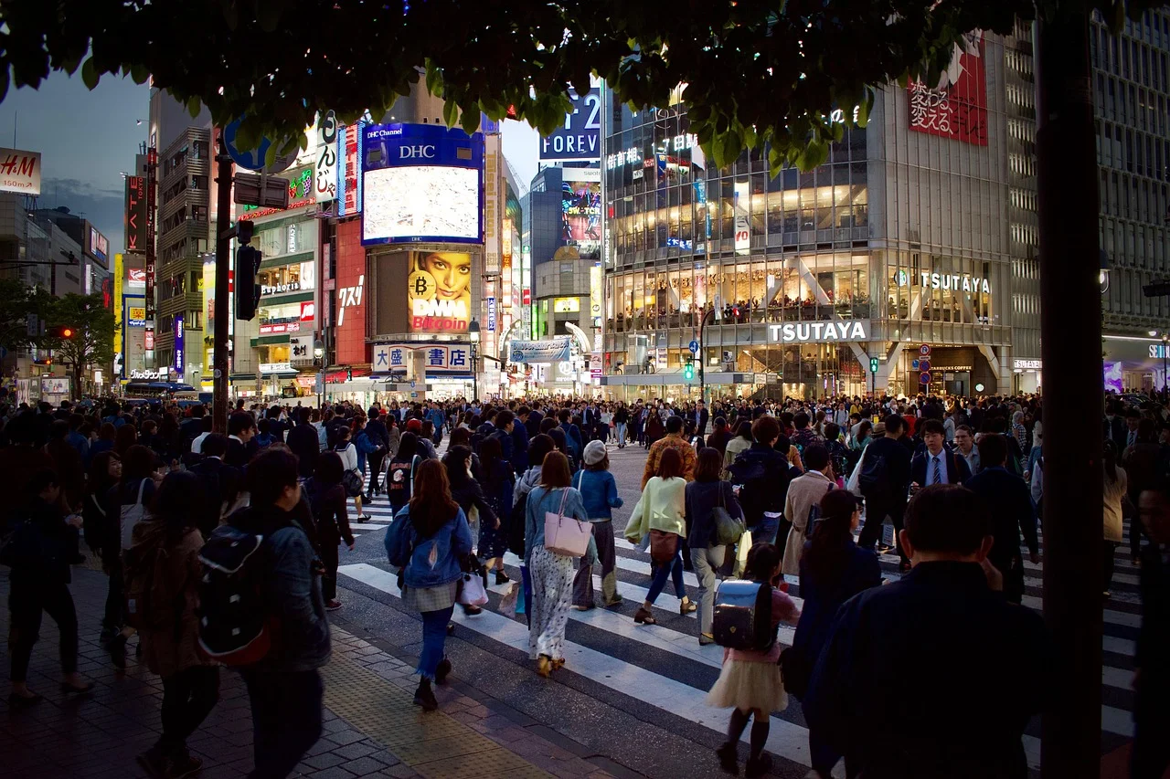 Foule traversant le carrefour de Shibuya à Tokyo au crépuscule, enseignes lumineuses et écrans publicitaires en fond