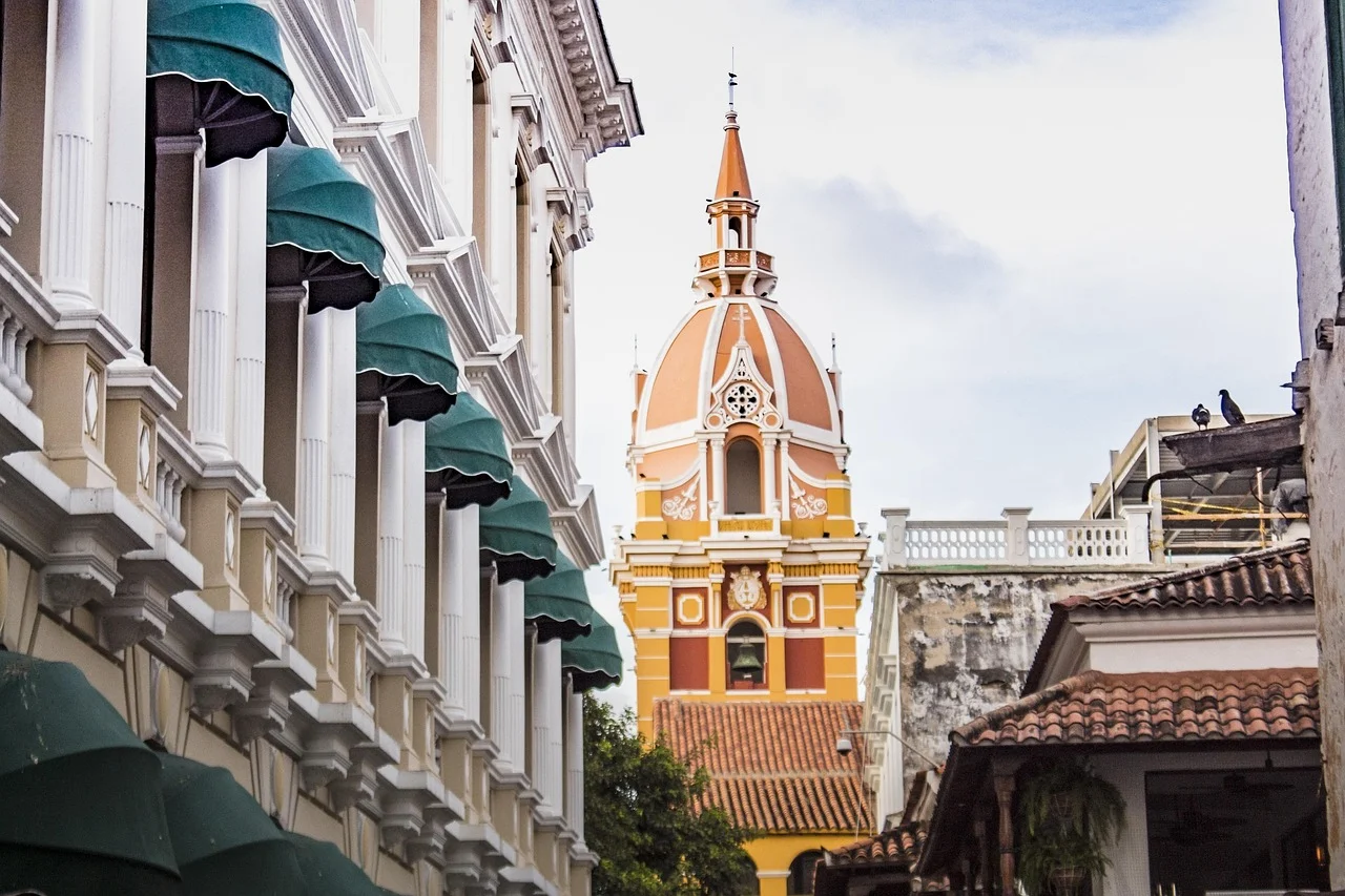 Le clocher jaune et orange de la cathédrale de Carthagène des Indes entre les balcons blancs et les stores verts d'une rue coloniale