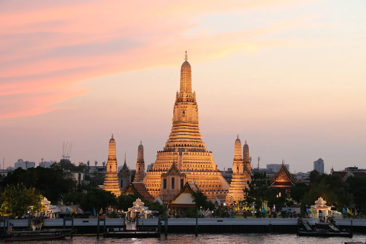 Le temple Wat Arun illuminé au coucher du soleil sur la rive du fleuve Chao Phraya à Bangkok, ciel rose et orangé