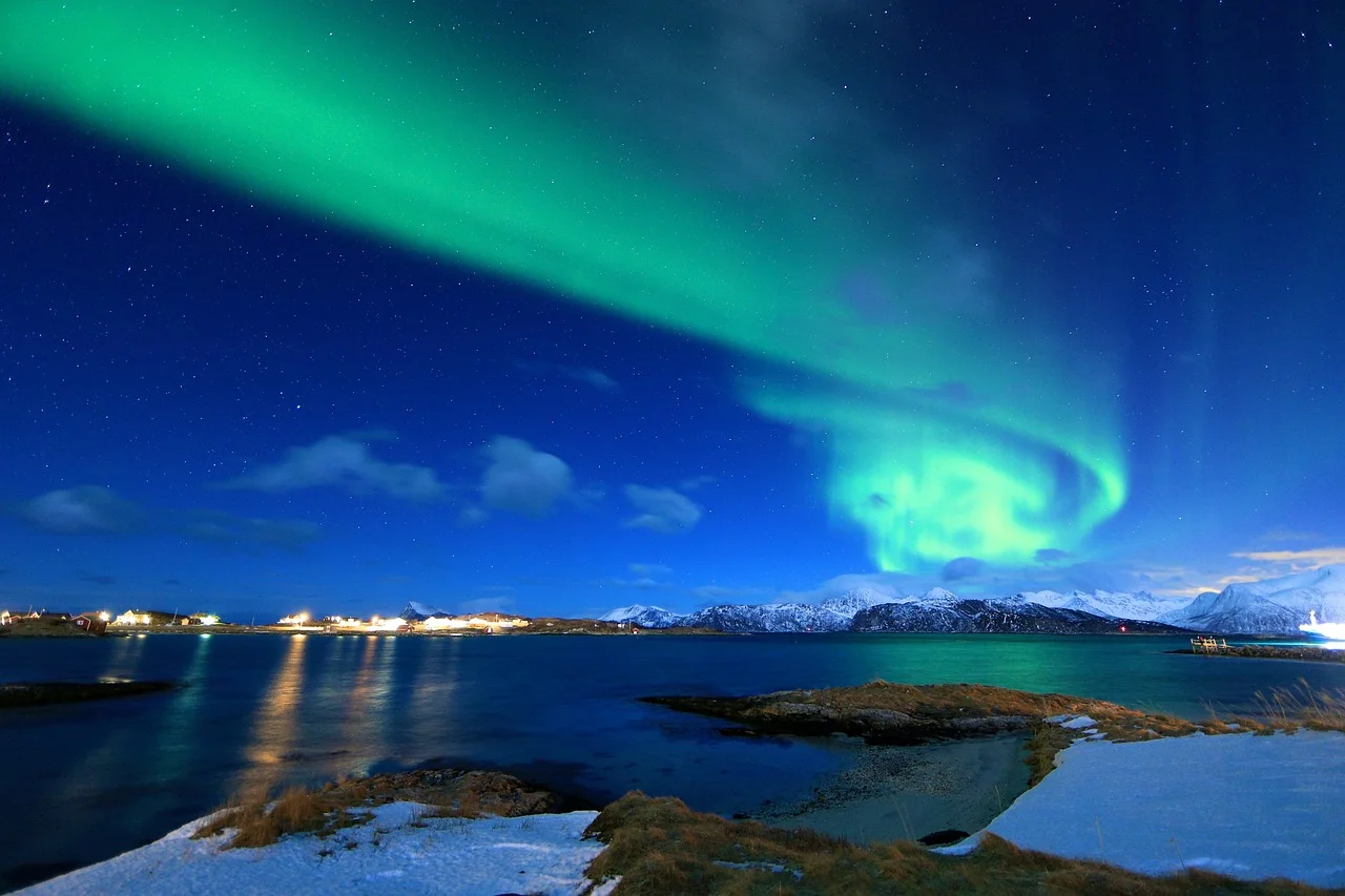 Longue draperie d'aurore boréale verte au-dessus d'un fjord gelé et de montagnes enneigées près de Tromsø, en Norvège du Nord.