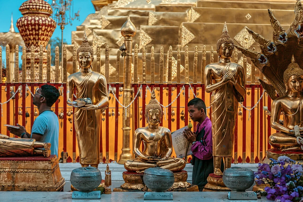 Rangée de statues de Bouddha dorées et fidèles en prière devant le chedi doré du Wat Phra That Doi Suthep, à Chiang Mai.