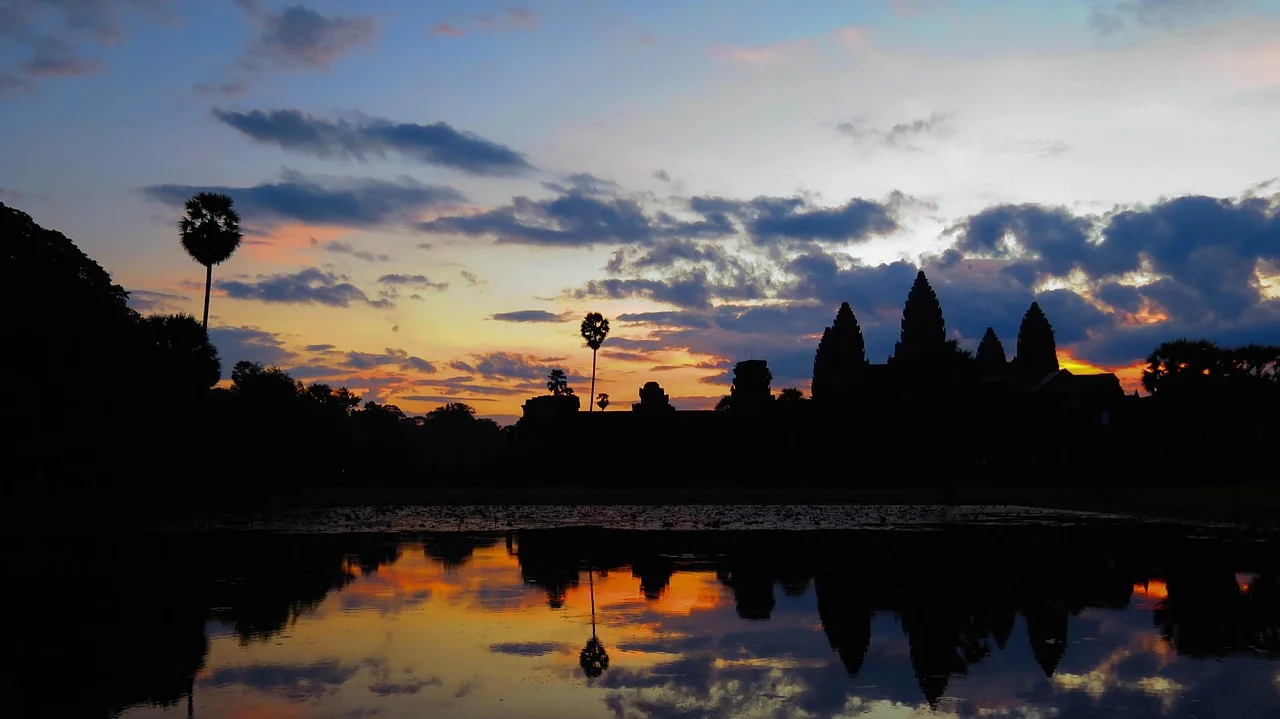 Silhouette des cinq tours d'Angkor Wat au lever du soleil, reflétées dans le bassin devant le temple, palmiers à sucre en contre-jour