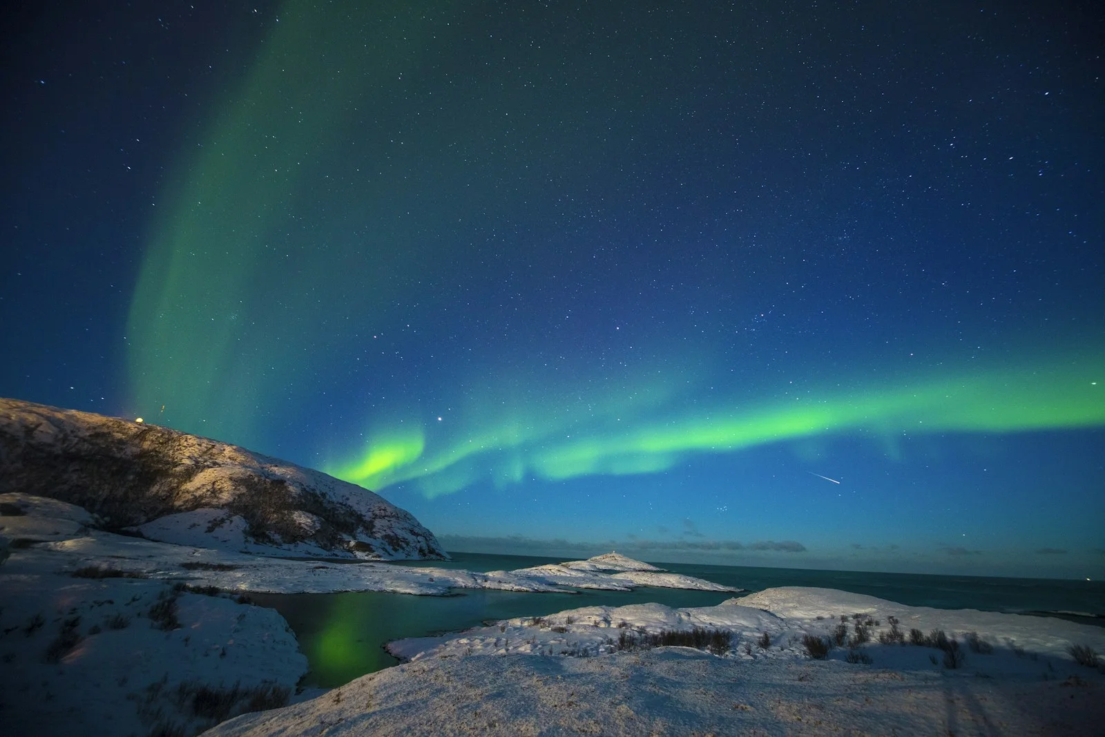 Aurore boréale verte au-dessus d'un rivage enneigé près de Tromsø, ciel étoilé
