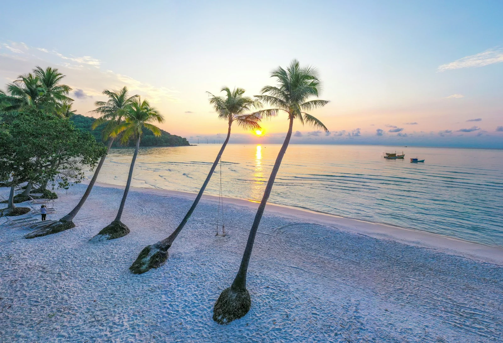 Cocotiers penchés sur la plage de Sao à Phú Quốc au coucher du soleil, mer calme et barques au large