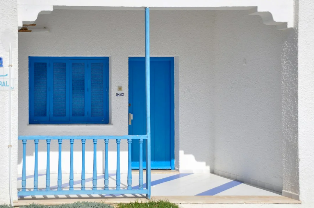 Façade blanche d'une maison de Tunis avec porte, volets et rambarde peints en bleu