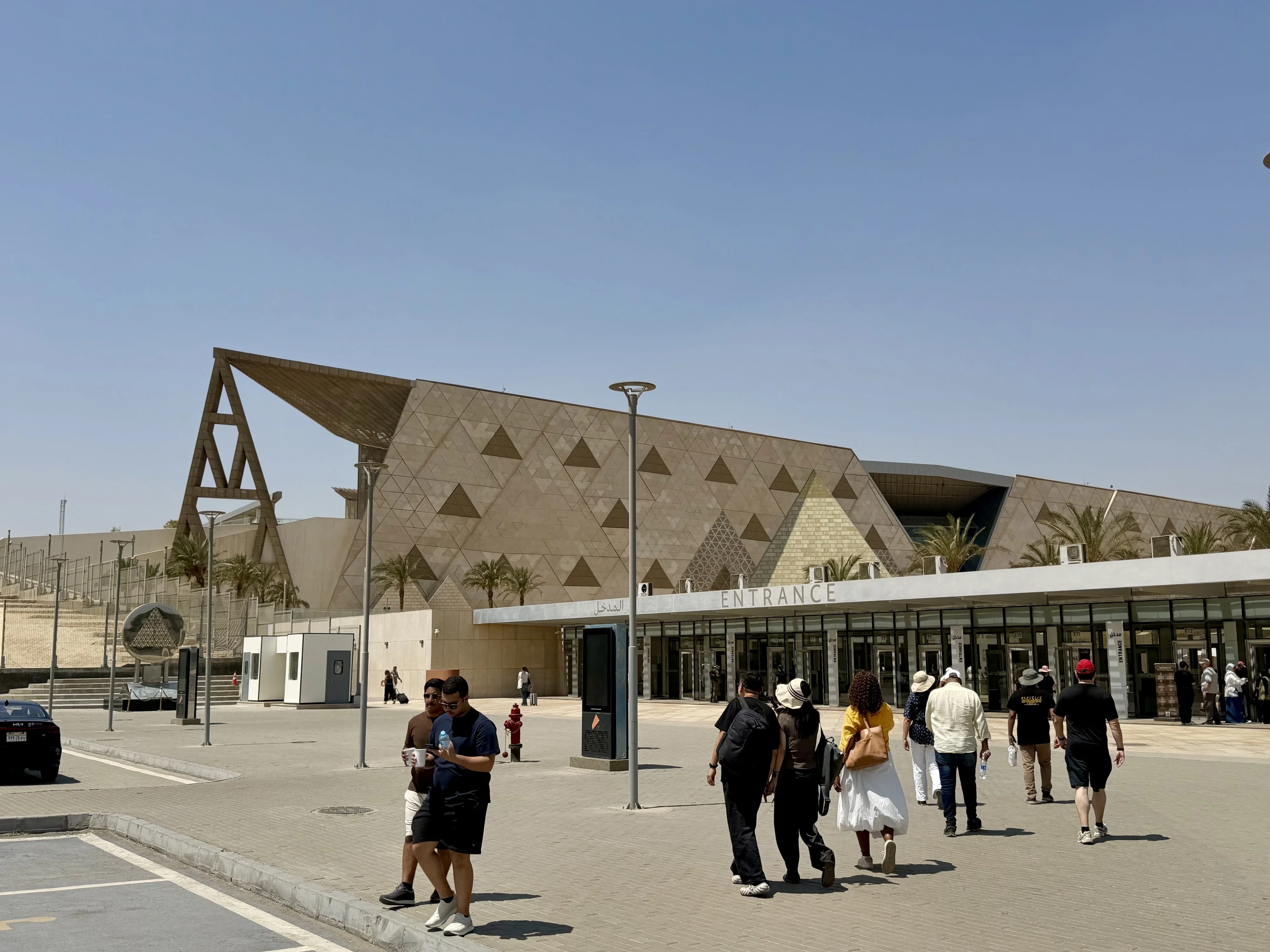Façade triangulaire du Grand Musée égyptien à Gizeh, avec des visiteurs sur le parvis