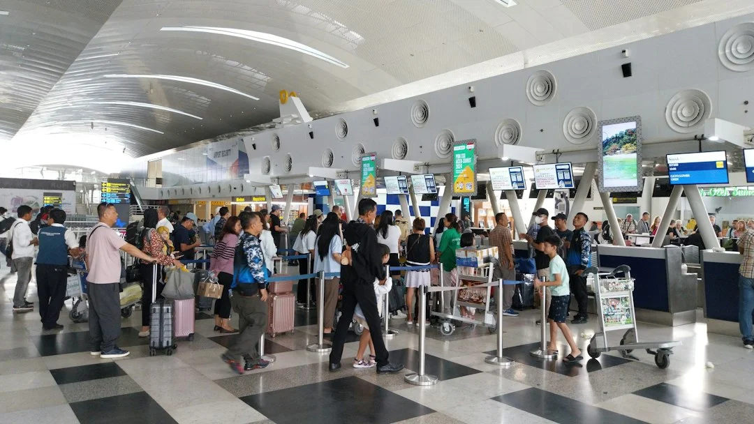 Hall d'enregistrement d'un aéroport avec des files de voyageurs et leurs valises devant les comptoirs des compagnies aériennes.