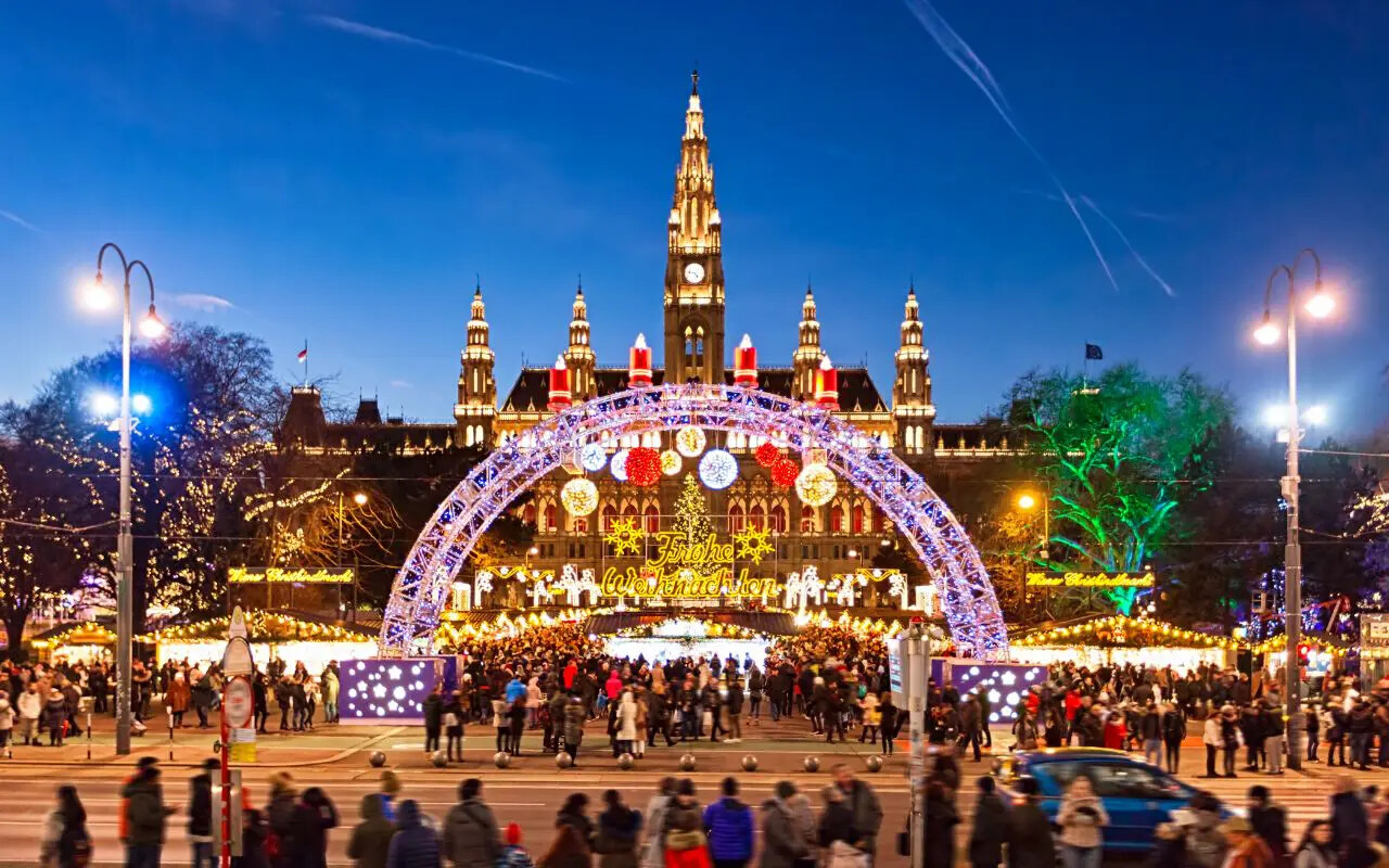 Marché de Noël de la Rathausplatz à Vienne, avec l'hôtel de ville néogothique illuminé et une arche lumineuse