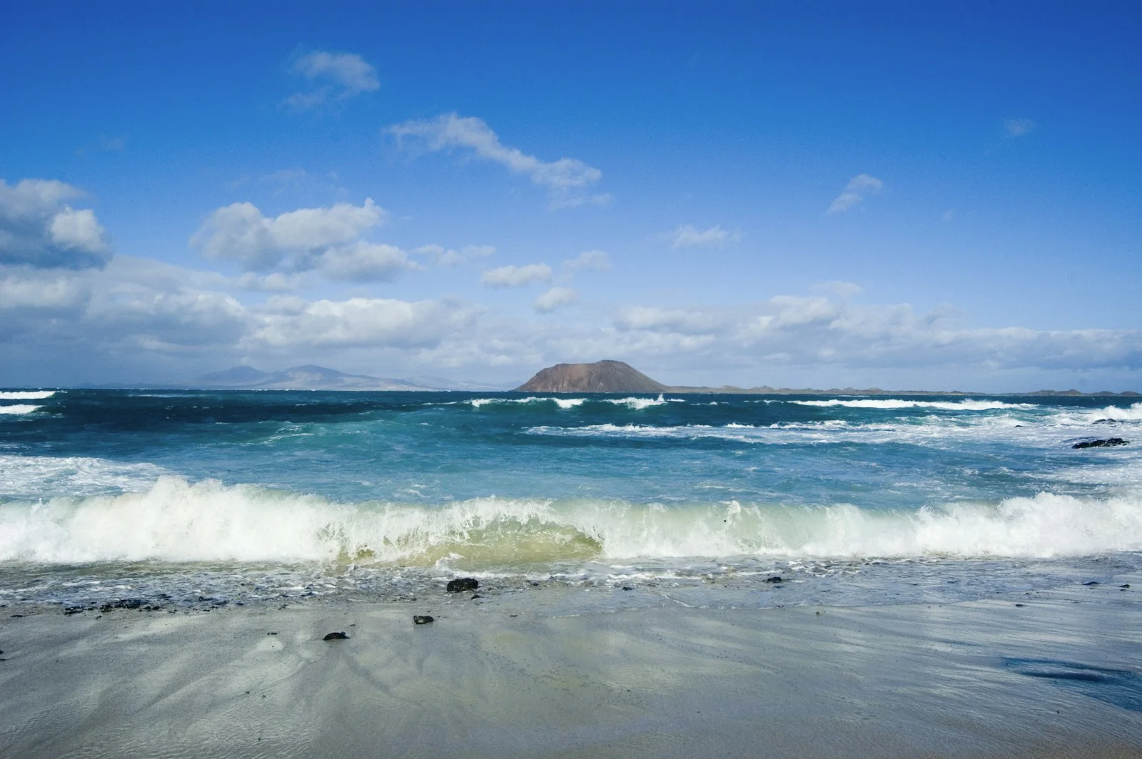 Plage de Corralejo à Fuerteventura, vagues turquoise et l'île de Lobos à l'horizon sous un ciel bleu
