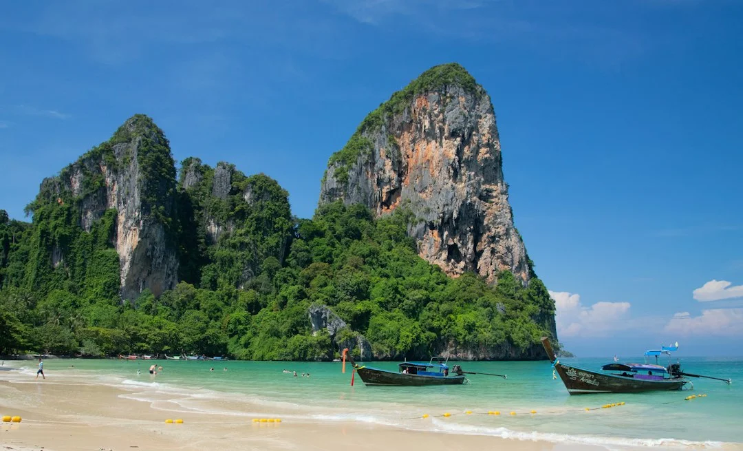 Plage de Railay à Krabi, falaises calcaires couvertes de jungle et bateaux longtail sur l'eau turquoise