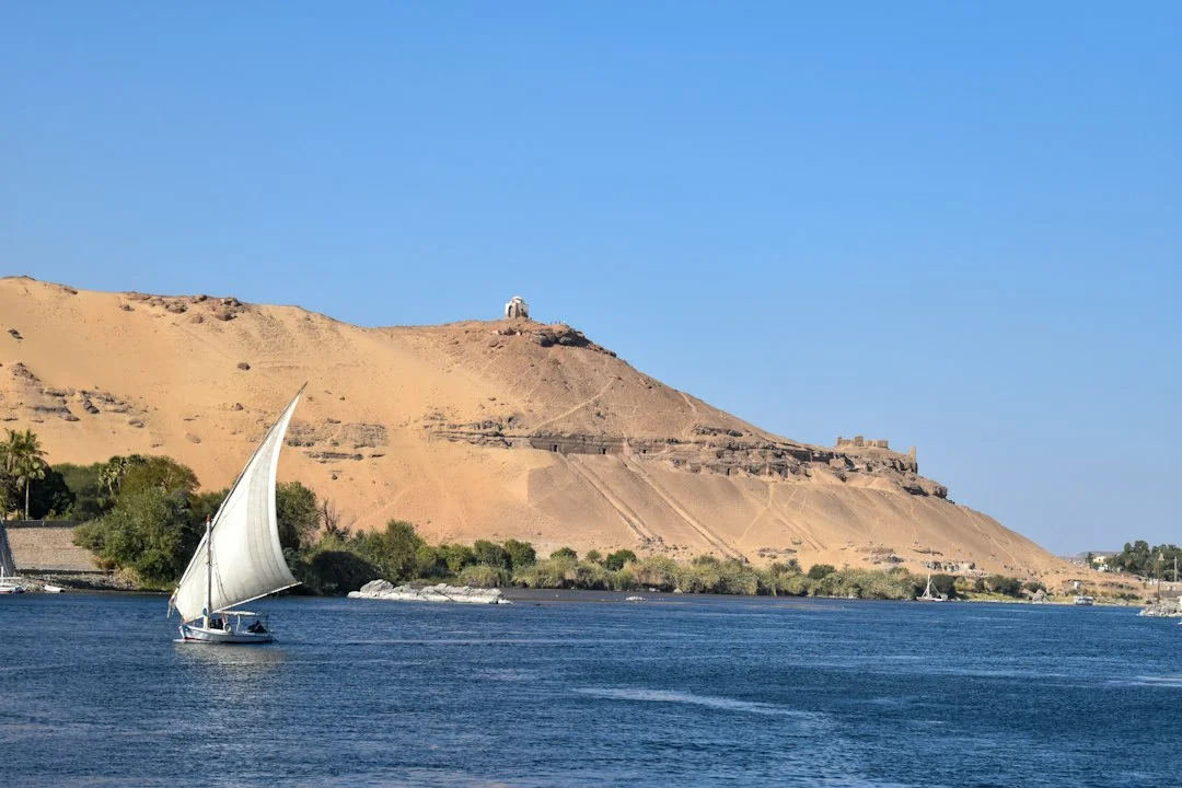 Une felouque blanche sur le Nil à Assouan, devant la colline dorée de la rive ouest